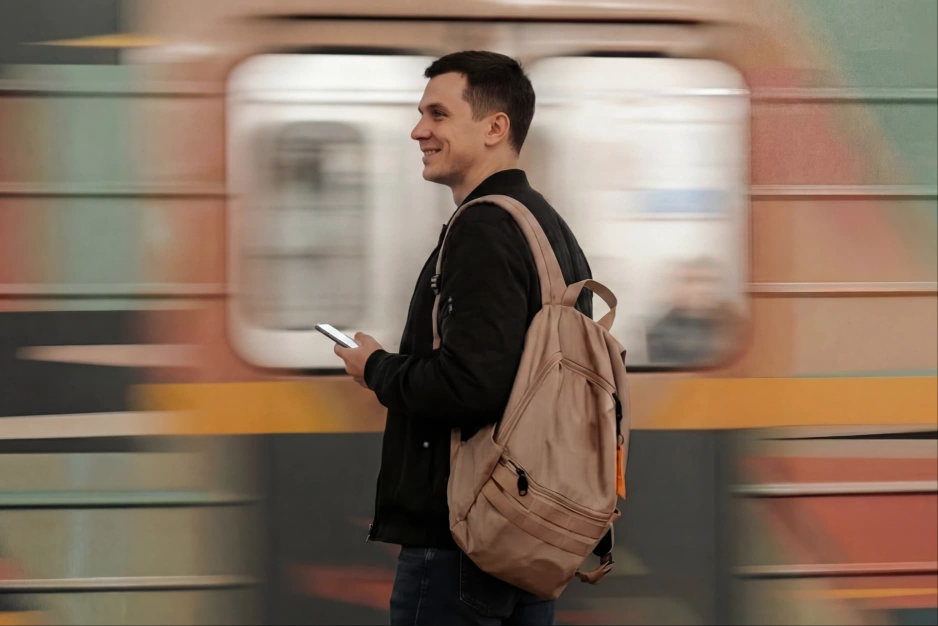 A young man checking his phone as a subway train rushes past behind him