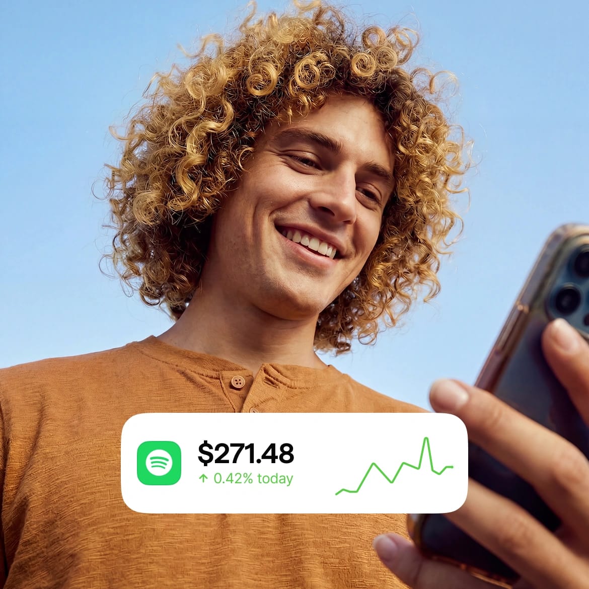 Man smiling at his phone showing Spotify stock up 0.42% to $271.48